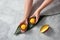 Woman hands holding natural mango ice cream in the coconut shell with half fresh mango on palm leaves on gray stone