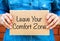 Woman hands holding piece of cardboard with phrase Leave Your Comfort Zone