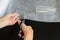 Woman hands holding a scissors and cutting a piece of white transparent bubble wrap for to wrap up a glass. On a black background