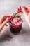 Woman hands holds currant berries for preparation of fresh ice cold fruit cocktail drink in glass with rosemary leaf