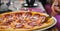 Woman hands with knife and fork cutting pepperoni pizza on table