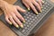 Woman hands on a laptop keyboard on brown table. She working, typing something. Yellow nail polish on her fingers