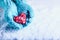 Woman hands in light teal knitted mittens are holding beautiful entwined vintage red heart in a snow. St. Valentine concept.