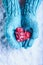 Woman hands in light teal knitted mittens are holding beautiful entwined vintage red heart in a snow. St. Valentine concept.