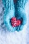 Woman hands in light teal knitted mittens are holding beautiful entwined vintage red heart in a snow. St. Valentine concept.