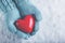 Woman hands in light teal knitted mittens are holding beautiful glossy red heart in snow background. Love, St. Valentine concept