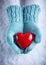 Woman hands in light teal knitted mittens are holding a beautiful glossy red heart in a snow. Love and St. Valentine concept
