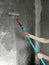 Woman hands with a long-handled roller applying a primer to the gray empty wall