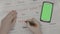 Woman hands marking period dates on calendar planning birth control while looking at smartphone with green screen on her desk -