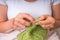 Woman hands with needles knitting with green wool