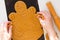 Woman hands removing excess dough after cutting out gingerbread man on raw dough on black teflon baking sheet on the