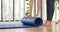 Woman hands rolled up yoga mat on gym floor in yoga fitness training room. Home workout woman close up hands rolling foam yoga gym