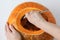 Woman hands scooping out seeds from inside of pumpkin using spoon on the white background