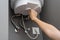 Woman hands setting temperature of water in heater electric boiler. Interior details close-up.