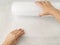 Woman hands unwind a roll of white transparent bubble wrap on a rough white background. Material for packing fragile items for