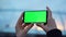 Woman hands using smartphone with green screen outdoors. Lady holding cellphone