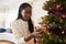 Woman Hanging Decorations On Christmas Tree At Home