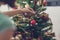 Woman hanging shiny red holiday bauble on Christmas tree inside. Over the shoulder view