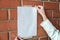 woman hangs a blank sheet of paper on a brick wall. blank ad mockup