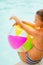 Woman in hat with beach ball sitting at poolside