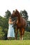 Woman in hat stay beside brown horse