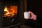 Woman having a hot cup of rink at the fireplace. Burning fireplace with wooden logs burning inside in the background. Warm