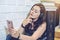 Woman in headphones listening to an audiobook on a phone sitting on wall background