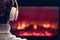 Woman in headphones sitting and warming at winter evening near fireplace flame.