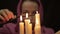 Woman in a headscarf doing the magic ritual. close-up several candle and old book. halloween or religion concept