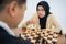 Woman in headscarf holding chess pieces moves while playing chess