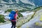 Woman with heavy backpack and a rolled sleeping pad, navigating a trekking trail in Retezat mountains part of Carpathians.