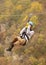 A woman in a helmet flies on a zipline over a colorful autumn gorge