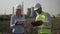 Woman with helmet noting in her notebook working progress report of young engineer using tablet pc near refinery platform -