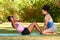 Woman helps her friend with sit up crunches, assist in park, fitness buddy