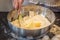 Woman in her apron kneads the dough in a metal bowl of egg ingredients, flour, butter. Flour on a black wooden table. On