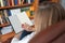 Woman with her back sitting in an armchair with a large bookcase full of books in front of her.