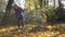 Woman and her girl daughter raking leaves in yard. Little child mother helper