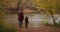 Woman with her little child at nature, people are standing on coast of picturesque forest pond at autumn day