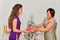 Woman hiding a golden wrapped gift box gives a silver wrapped gift box to an asian woman near a Christmas tree. Christmas holiday