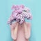 Woman hiding head in bouquet lilac flowers over colorful blue