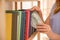 Woman hiding money between books on shelf indoors. Financial savings