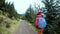 Woman hiker with backpack, wearing in red jacket and orange pants, walking on the mountains background