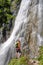 Woman hiker, with a green backpack, looks up at Dalfazer waterfall, Austria