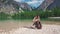 Woman hiker with photocamera sits on the shore of Lago di Braies, Dolomites, Italy