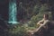 Woman hiker sitting near waterfall in deep forest.