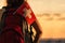 Woman hiker on the top of mountain in shorts and a t-shirt with a backpack and flag of Switzerland on a sunset sky background.