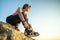 Woman hiker tying shoe laces of her sport boots while climbing steep big rock on a sunny day. Young female climber overcomes