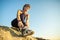 Woman hiker tying shoe laces of her sport boots while climbing steep big rock on a sunny day. Young female climber overcomes