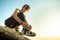 Woman hiker tying shoe laces of her sport boots while climbing steep big rock on a sunny day. Young female climber overcomes