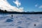 Woman with hiking backpack on field of deep crystal snow with scenic view of frozen alpine lake Forstsee, Techelsberg, Austria